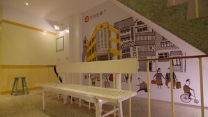 Um quarto com um banco branco, uma escada verde e um mural na parede retratando edifícios e pessoas.