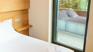 Ein Hotelzimmer mit Bett, Holz-Kopfteil, Schiebeglasdoor zum Balkon und Blick auf Grünfläche.