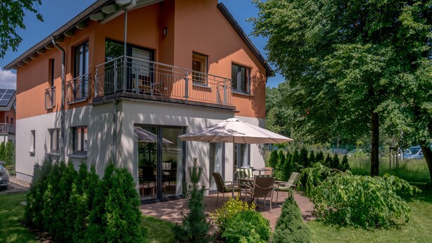 A two-story house with a balcony, a patio with outdoor furniture, and a well-maintained garden. - Ferienpark Rübezahl am Müggelsee (Berlin)