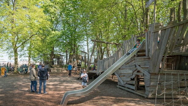 A playground with a wooden slide and climbing structures, surrounded by trees. - Ferienpark Rübezahl am Müggelsee (Berlin)