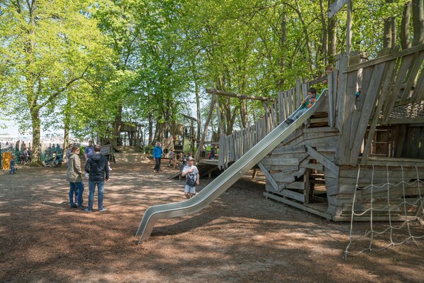 A playground with a wooden slide and climbing structures, surrounded by trees. - Ferienpark Rübezahl am Müggelsee (Berlin)