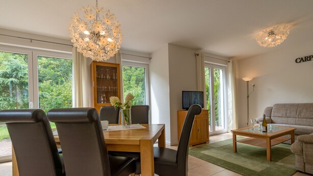 A modern living room with a dining area, large windows, and a chandelier. - Ferienpark Rübezahl am Müggelsee (Berlin)