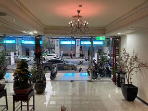 Un hall d’hôtel agrémenté d’un lustre, de plantes en pot et offrant une vue sur la rue.