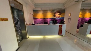 Zona de recepción de un hotel con diseño moderno, que incluye un mostrador de recepción, una pantalla digital y un mural en la pared.
