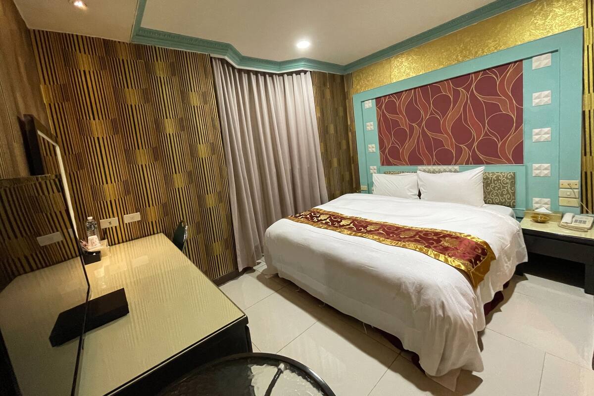 Une chambre d’hôtel comprenant un lit, un bureau, une chaise et une table de chevet avec un téléphone et une lampe.
