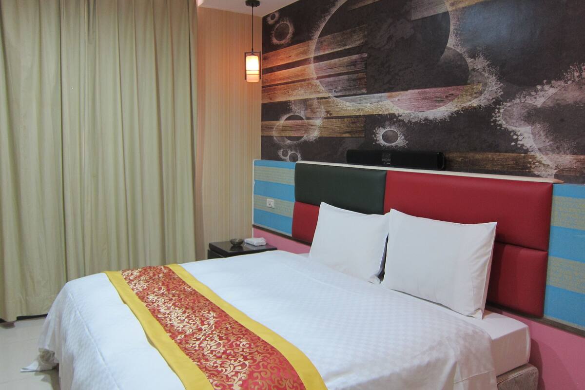 Une chambre d’hôtel avec un lit, une table de chevet, une lampe et un grand tableau abstrait accroché au mur.