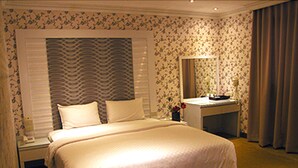 Una habitación de hotel con una cama grande, una mesita de noche, un espejo y un aparador.
