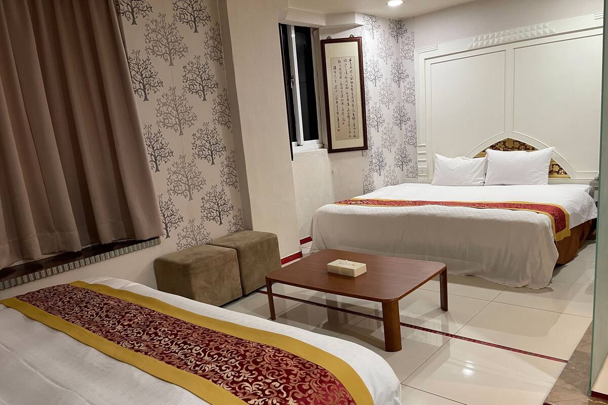 Une chambre d’hôtel avec deux lits, une petite table, un canapé et un mur décoratif.