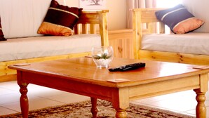 A wooden coffee table with a glass vase and remote control, a wooden chair, and a sofa with cushions in a living room. - Sunset Cottage- Noordhoek (Cape Town)