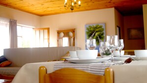 A dining area with a wooden ceiling, a sofa, and a table set for a meal. - Sunset Cottage- Noordhoek (Cape Town)