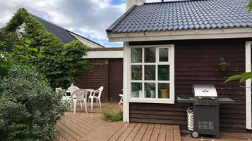 A wooden deck with a barbecue grill and a window overlooking a garden.