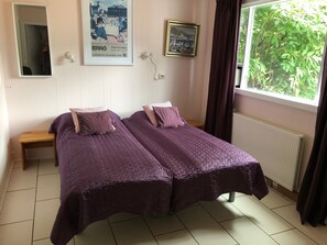 A room with two beds, a wooden nightstand, a poster on the wall, a window with curtains, and a radiator. - Big Villa in Húsavík Suburb (Husavik)