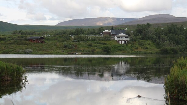 Un lac bordé de maisons, entouré de verdure et avec des montagnes en arrière-plan.