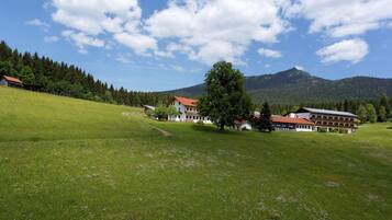 Entorno rural con un edificio grande, posiblemente un hotel, rodeado de campos verdes y una montaña al fondo.