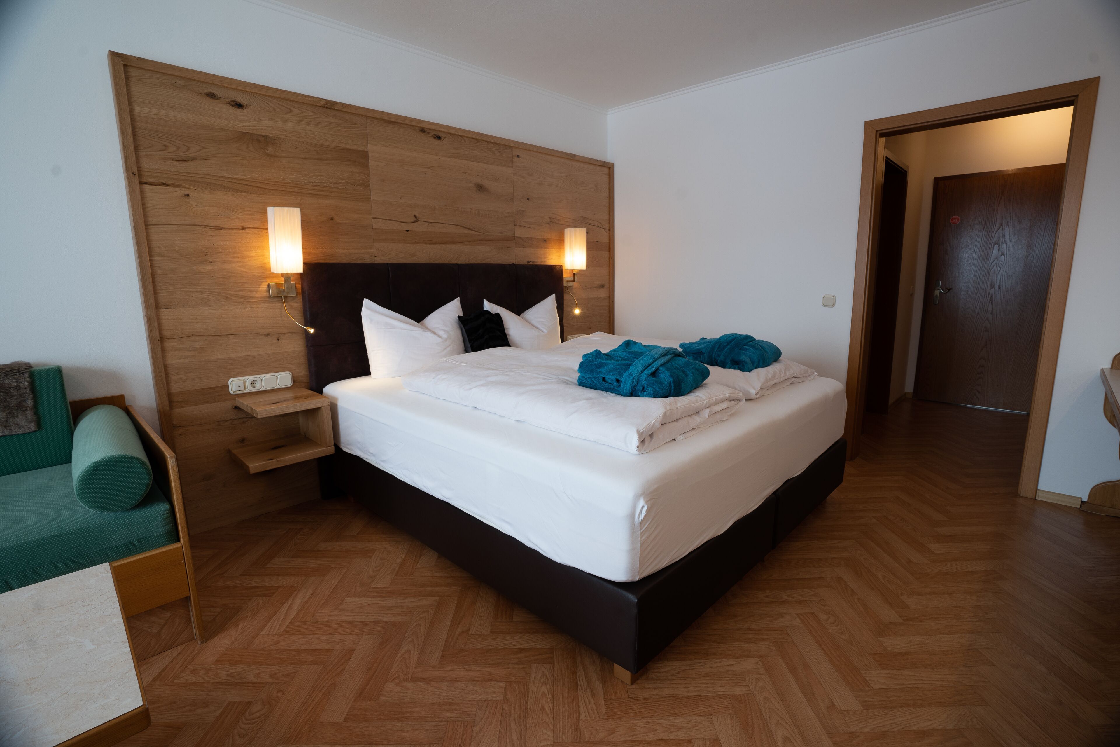 A bedroom with a wooden headboard, a bed with white bedding, a bedside table, and a nightstand.