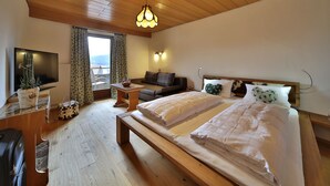 A bedroom with a wooden ceiling, a bed with white bedding, a TV, a small table with a plant, and a view of the outdoors. - Osserhotel (Lohberg)