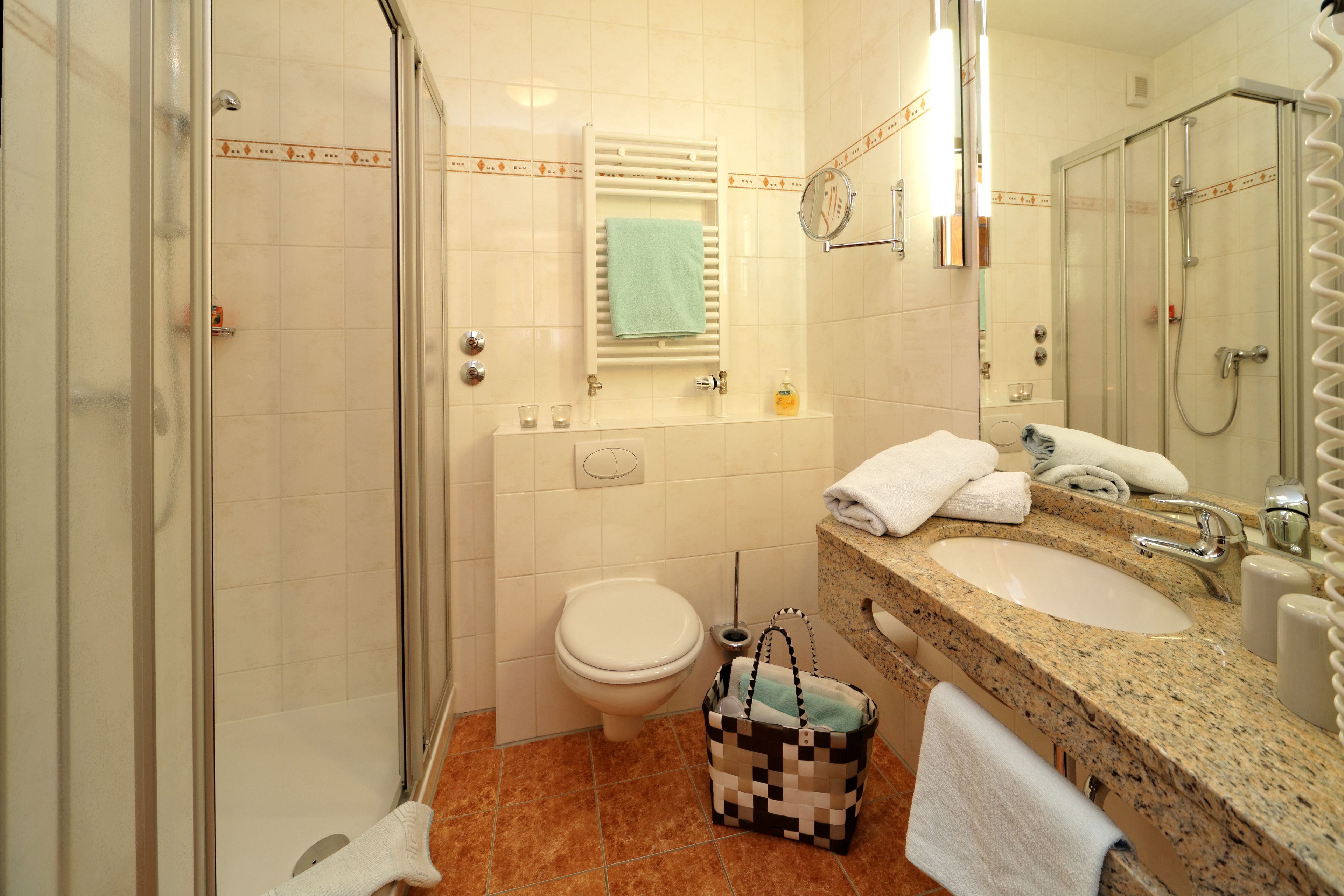 Een badkamer met een douchecabine van glas, een toilet, een wastafel met een granieten aanrechtblad en een spiegel.