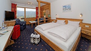 A hotel room with a large bed, a desk with a TV, a chair, a small table, and a view of the mountains. - Osserhotel (Lohberg)