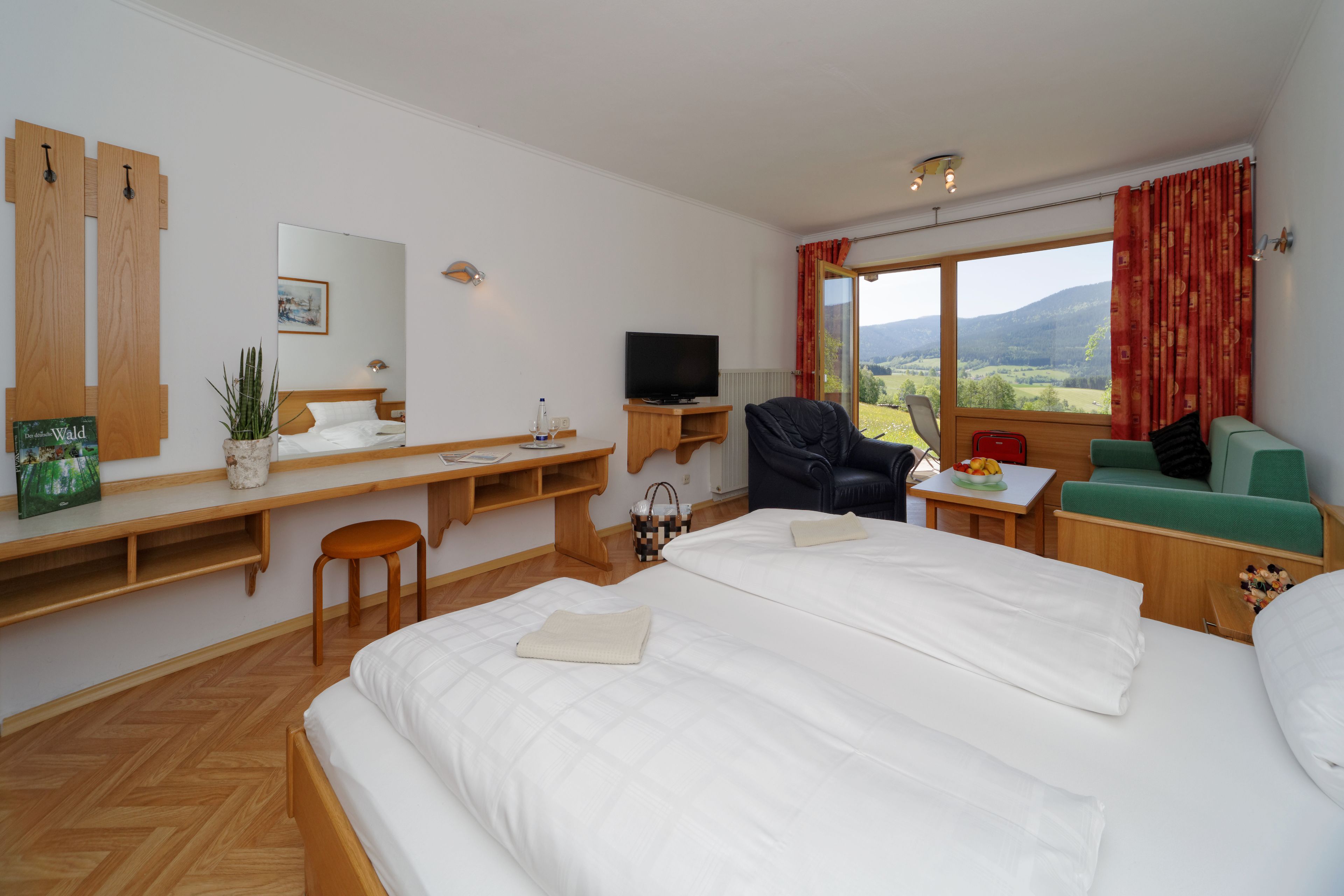 Ein Hotelzimmer mit einem großen Bett, einem Schreibtisch mit Computer, einem Fernseher und Blick ins Freie.