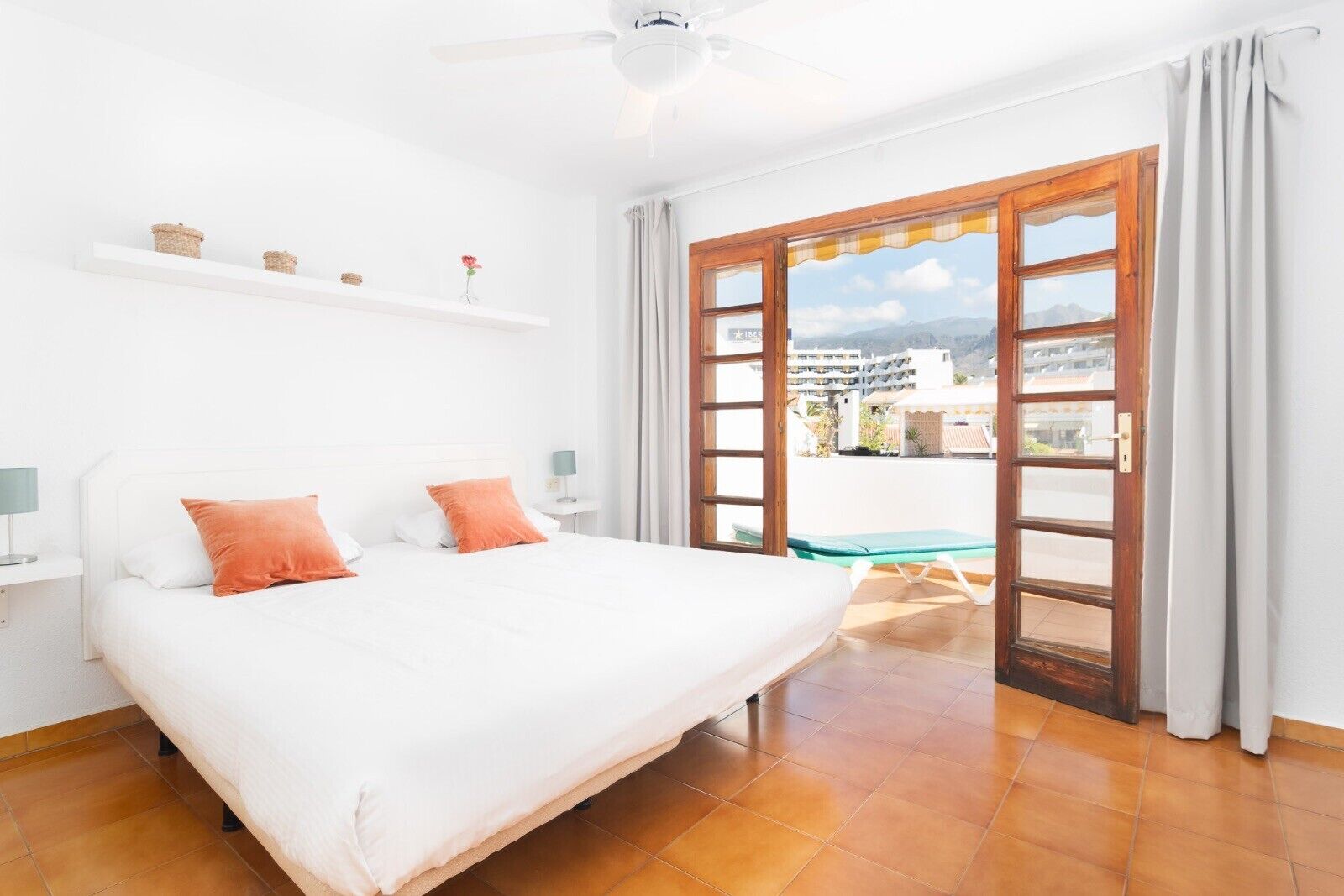 A bedroom with a bed, a nightstand, a ceiling fan, a window with curtains, and a view of the outside.
