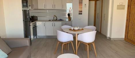 Una cocina moderna con armarios blancos, una mesa de comedor con sillas, un sofá y un control remoto en el suelo.