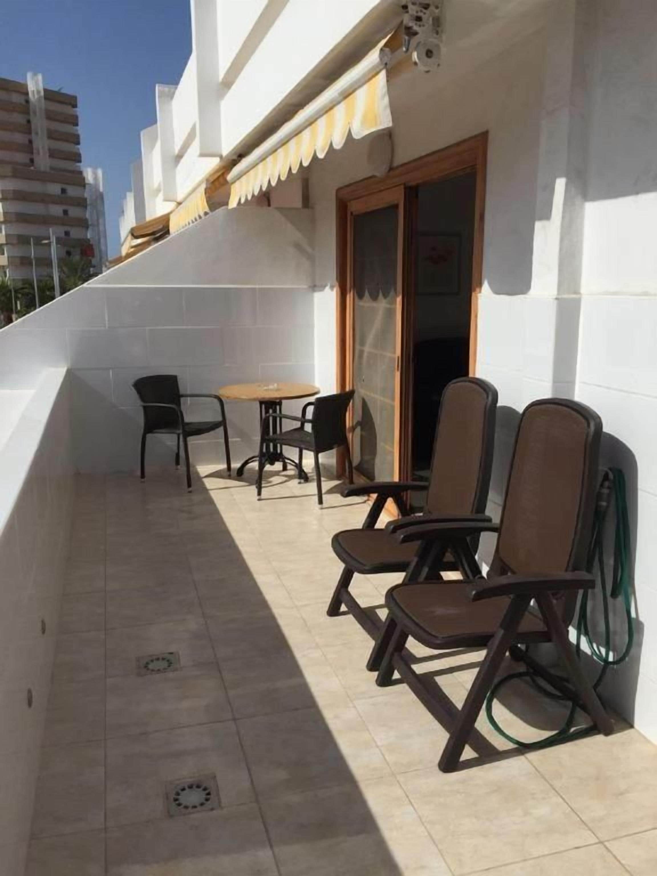 A balcony with a table and chairs, a door, and a green garden hose.