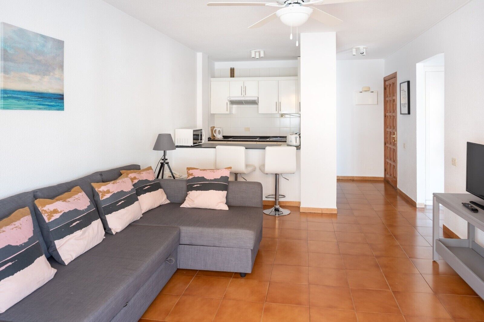 A modern living room with a grey sectional sofa, a TV stand, and a kitchen in the background.