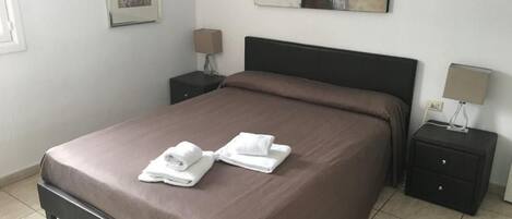 A neatly made bed with a brown bedspread, two bedside tables with lamps, and a framed picture on the wall.