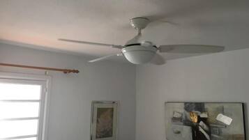 A room with a ceiling fan, a window with blinds, and two framed artworks on the wall.
