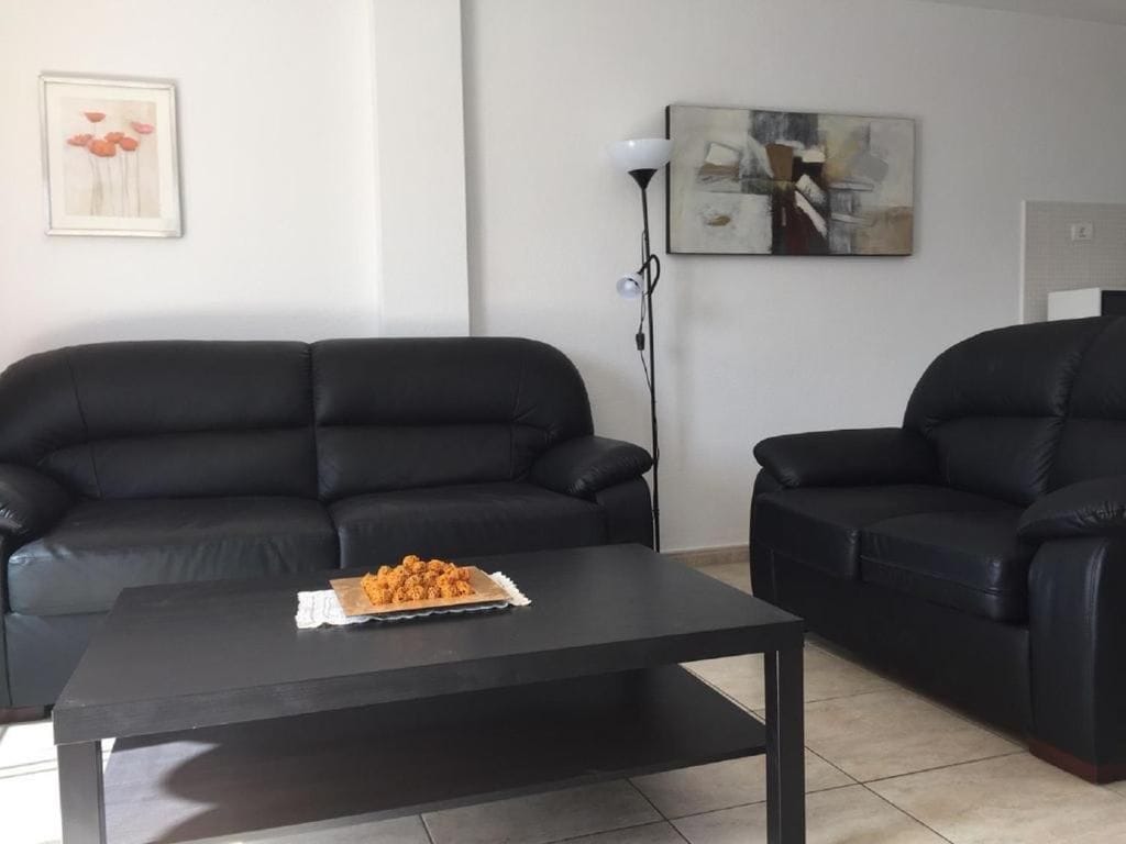 A living room with two black leather sofas, a black coffee table, a framed picture on the wall, and a floor lamp.