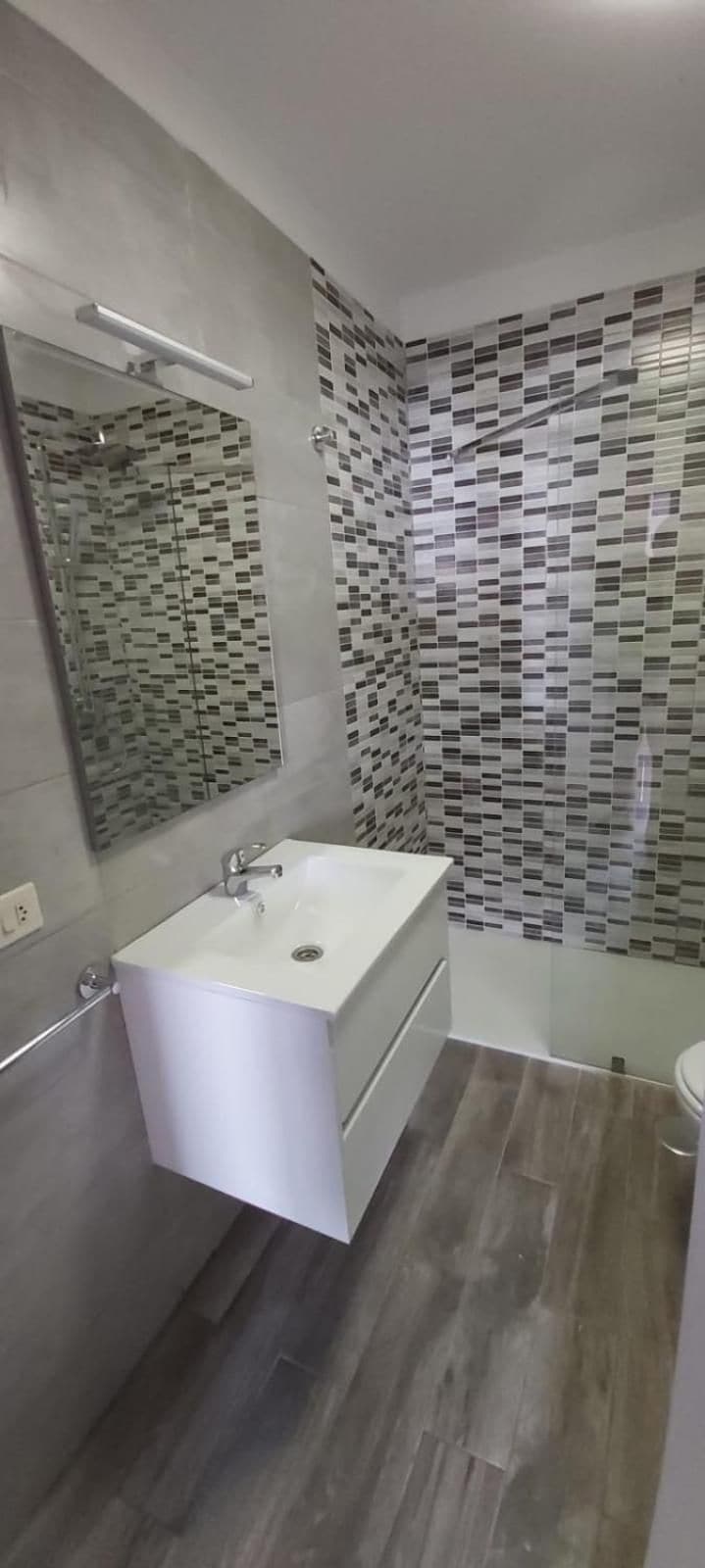 Un baño moderno con tocador blanco, cabina de ducha con mampara de vidrio y paredes con azulejos estampados.