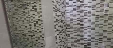Un baño moderno con tocador blanco, cabina de ducha con mampara de vidrio y paredes con azulejos estampados.