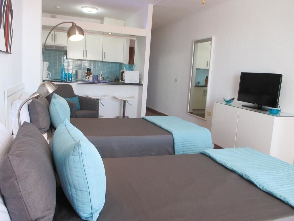 Ein Zimmer mit zwei Betten, einem Fernseher, einem Schreibtisch und einer Küchenzeile.