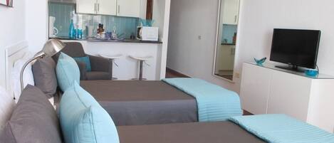 Ein Zimmer mit zwei Betten, einem Fernseher, einem Schreibtisch und einer Küchenzeile.