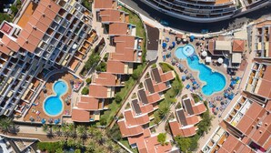 Vista aérea de un hotel con múltiples piscinas, un patio central y una estructura de edificio curva.