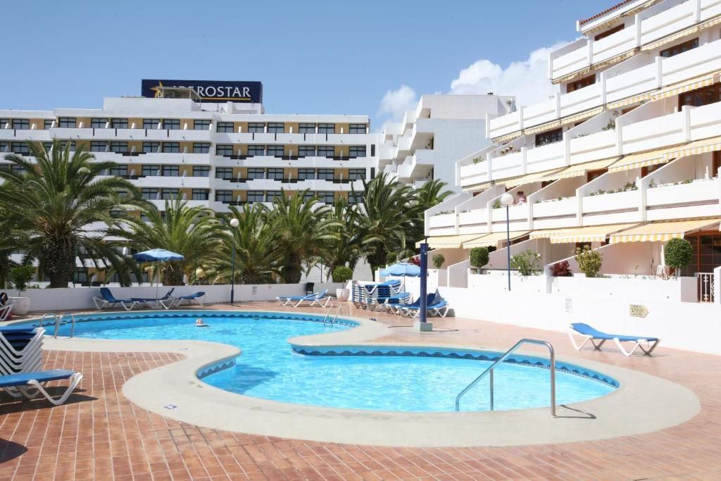 A hotel with a swimming pool, palm trees, and a sign that reads 'ROSTAR'.