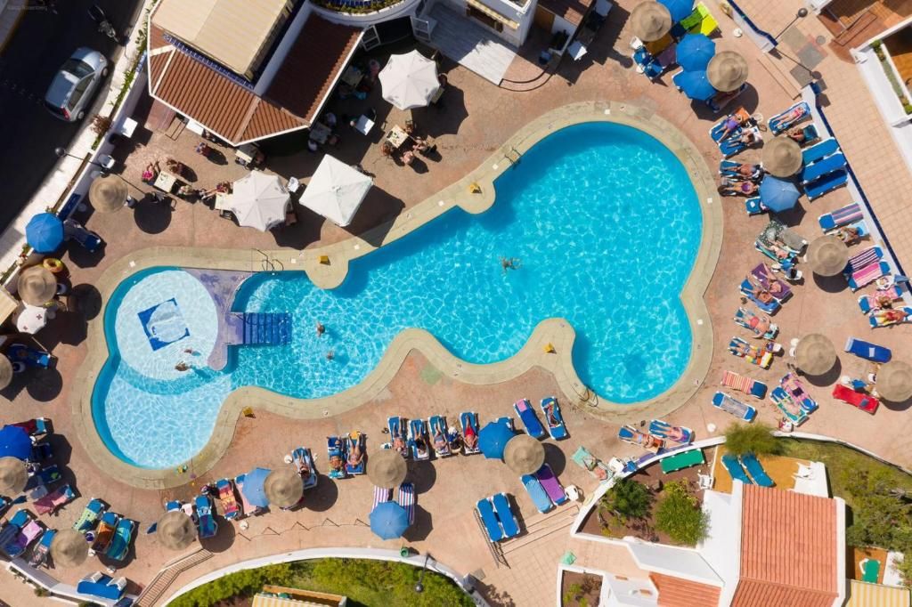 Una piscina con diseño ondulado, rodeada de sillones de descanso y sombrillas.