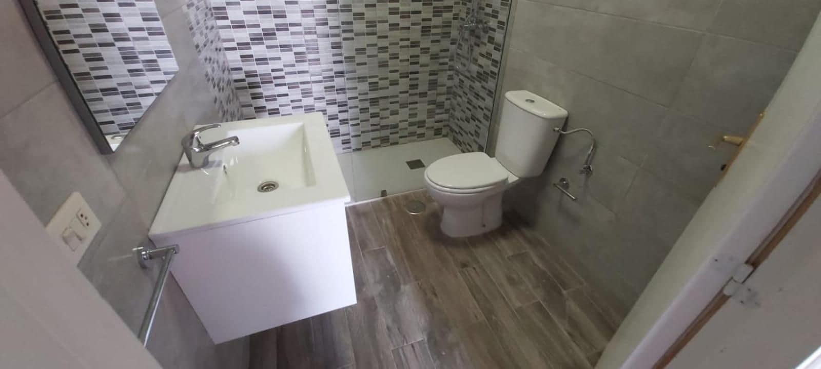 Un baño con lavamanos, inodoro y ducha blancos. El suelo está cubierto de baldosas y las paredes tienen un diseño de azulejos estampados.