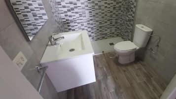 Un baño con lavamanos, inodoro y ducha blancos. El suelo está cubierto de baldosas y las paredes tienen un diseño de azulejos estampados.