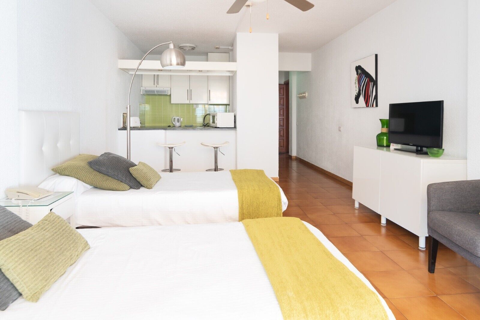 Una habitación de hotel con dos camas, una kitchenette, un televisor y un sofá.