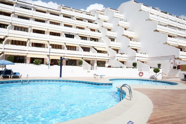 Un hotel con piscina, varios balcones y fachada blanca.