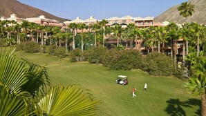 Un campo de golf con un club de campo, palmeras y montañas al fondo.
