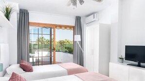Habitación de hotel moderna con dos camas, televisión y balcón con vistas a la vegetación.
