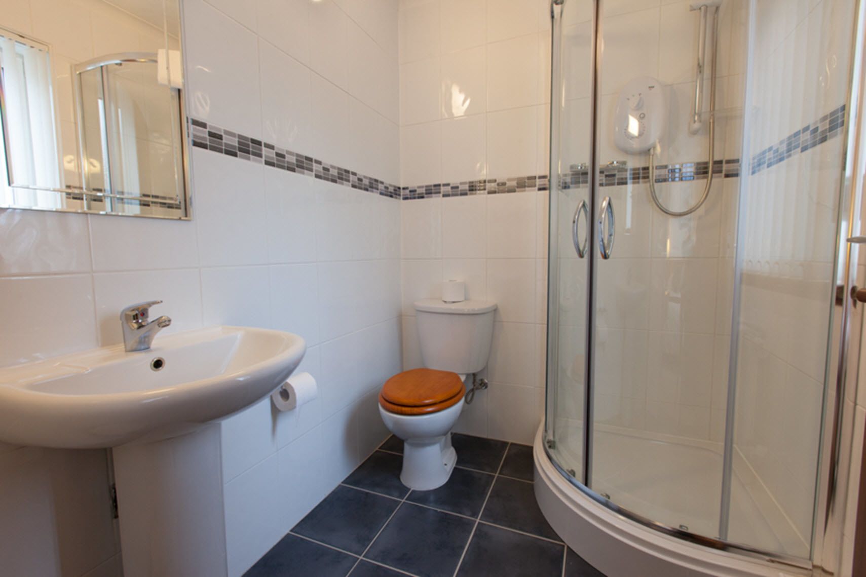 Baño con lavamanos, inodoro y ducha con mampara de vidrio.