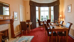 A formal dining room with a fireplace, a chandelier, and a view of the outdoors through large windows. - Cedars Guest House (Dunoon)