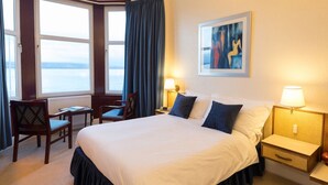 A hotel room with a large bed, two bedside tables, a chair, a desk, and a window with curtains. - Cedars Guest House (Dunoon)