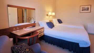 A hotel room with a bed, a desk with a chair, a mirror, and a wall-mounted lamp.