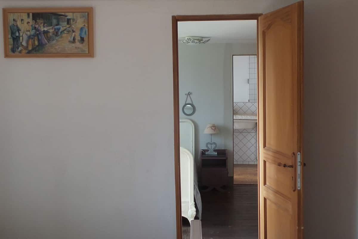 Quarto com cama, porta de madeira, pintura na parede e corredor que dá para outro cômodo.