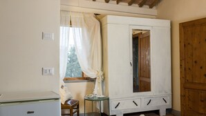Een kamer met een witte kledingkast, een klein tafeltje met een stoel en een raam met gordijnen.