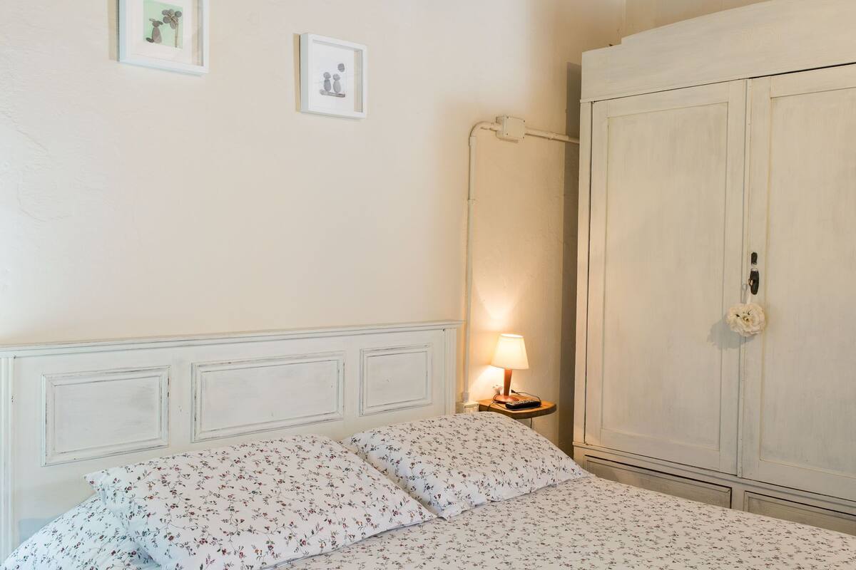 A bedroom with a bed, a nightstand with a lamp, and a wardrobe.